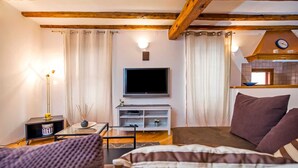 Una habitación acogedora con una cama, un televisor, una mesita con lámpara y un estante con adornos.