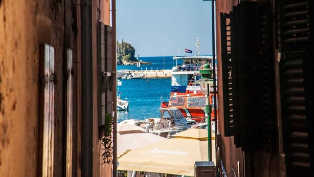 Una calle estrecha con barcos amarrados en un muelle, cielo azul despejado y vista a una isla distante.