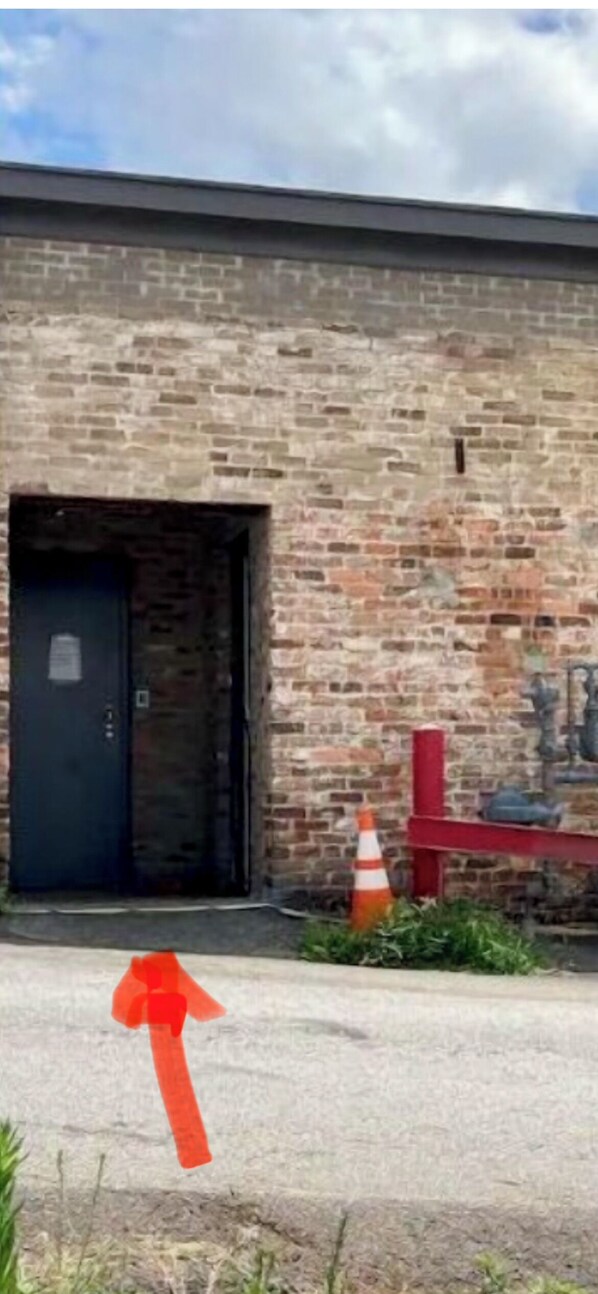 Un edificio de ladrillo con una puerta negra, una barandilla roja y un conos de tráfico.