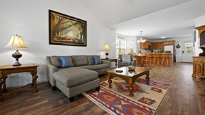 A living room with a sofa, coffee table, and rug, a dining area with chairs and a table, and a kitchen with cabinets and a refrigerator. - Bright and Breezy Riverfront Chalet (Pigeon Forge)