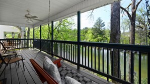 A covered porch with a view of a lake, wooden furniture, and a ceiling fan. - Bright and Breezy Riverfront Chalet (Pigeon Forge)