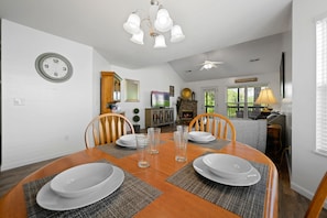 A dining area with a wooden table set for four, surrounded by chairs, and a clock on the wall.