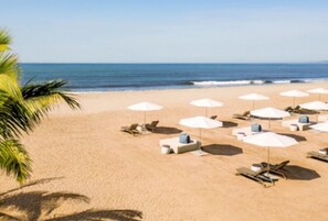 Een strand met witte parasols en ligbedden, palmbomen en de oceaan op de achtergrond.