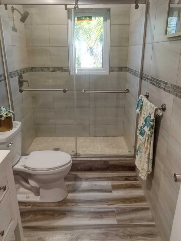 A bathroom with a shower, toilet, and a window. - Luxury Suites in Great Harbour Cay Bahamas, On the Bone Fish Grounds (Berry Islands)
