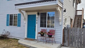 Ein Haus mit blauer Tür, Hausnummer 320, und zwei Blumenampeln an der Veranda.
