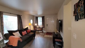 Ein Wohnzimmer mit Sofa, Fernseher, Lampe und einem Essbereich mit Tisch und Stühlen.