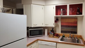 Una cocina compacta con armarios blancos, un microondas, un fregadero y un reloj rojo en la pared.
