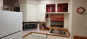 Una cocina compacta con armarios blancos, un microondas, un fregadero y un reloj rojo en la pared.