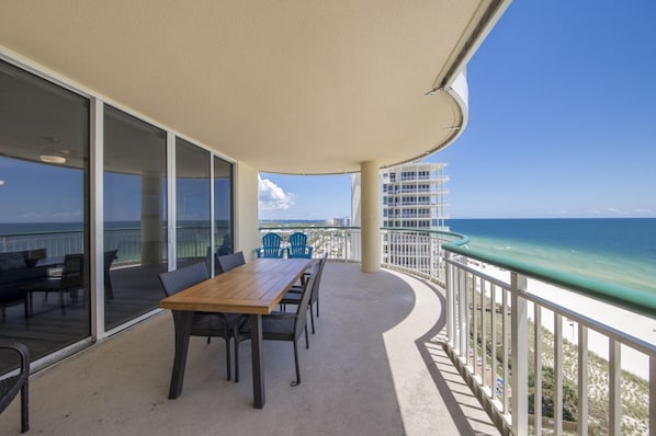 Un balcon avec une table et des chaises en bois, donnant sur une plage et l’océan.