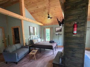 Une chambre confortable, aménagée dans le style d’un chalet, avec un lit, un canapé, une petite table et un ventilateur de plafond.