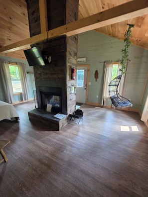 A spacious room with a fireplace, wooden floors, a hanging chair, and a television.