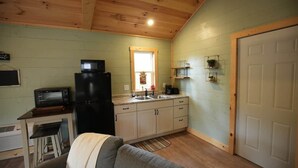 A compact kitchen with a refrigerator, microwave, sink, and a small dining area with a bench. - Firefly Landing at Avenwood Cabins (New Straitsville)
