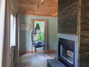 A room with a hanging chair, a fireplace, and a sign welcoming guests. - Firefly Landing at Avenwood Cabins (New Straitsville)