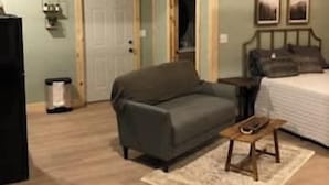A room with a wooden ceiling, a sofa, a bed, a small table, and a door. - Firefly Landing at Avenwood Cabins (New Straitsville)