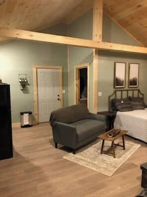 A room with a wooden ceiling, a sofa, a bed, a small table, and a door.