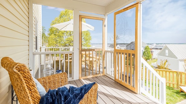 Ein überdachter Balkon mit Korbstühlen, einem Tisch und Blick auf eine Wohngegend.