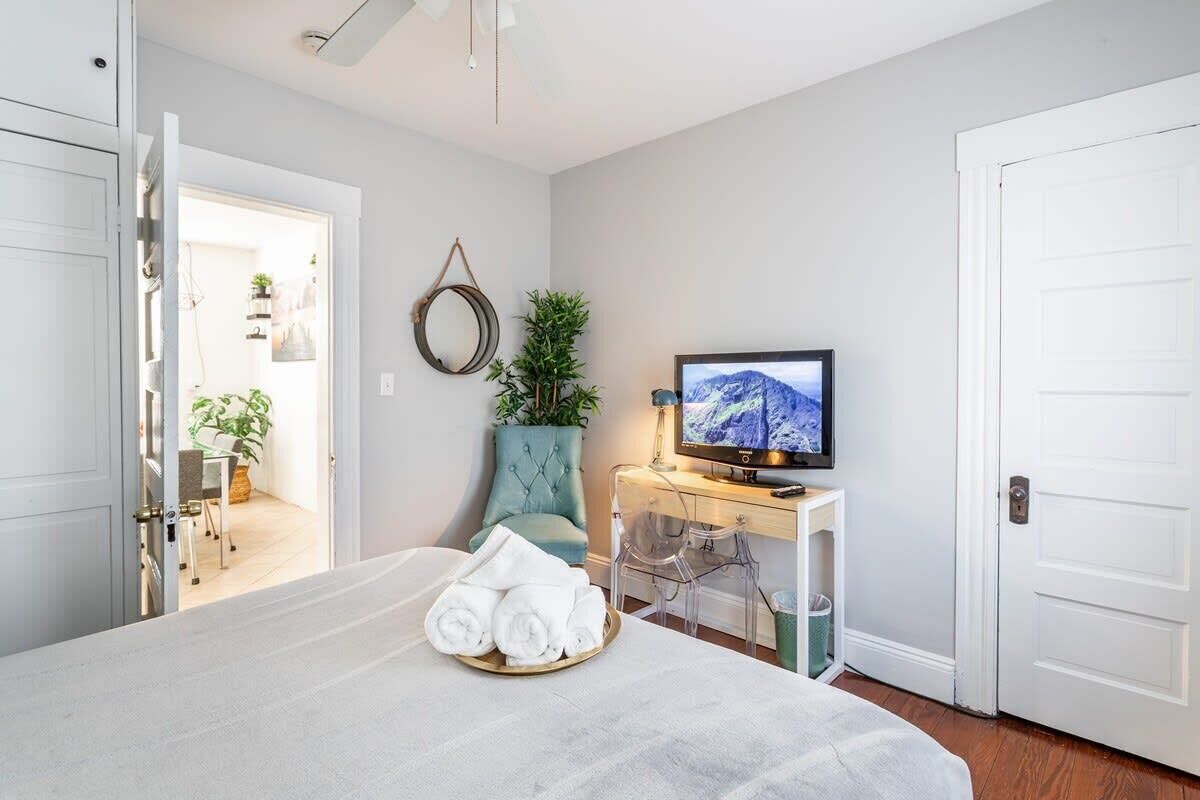 A hotel room with a bed, a TV, a desk with a computer, and a potted plant.