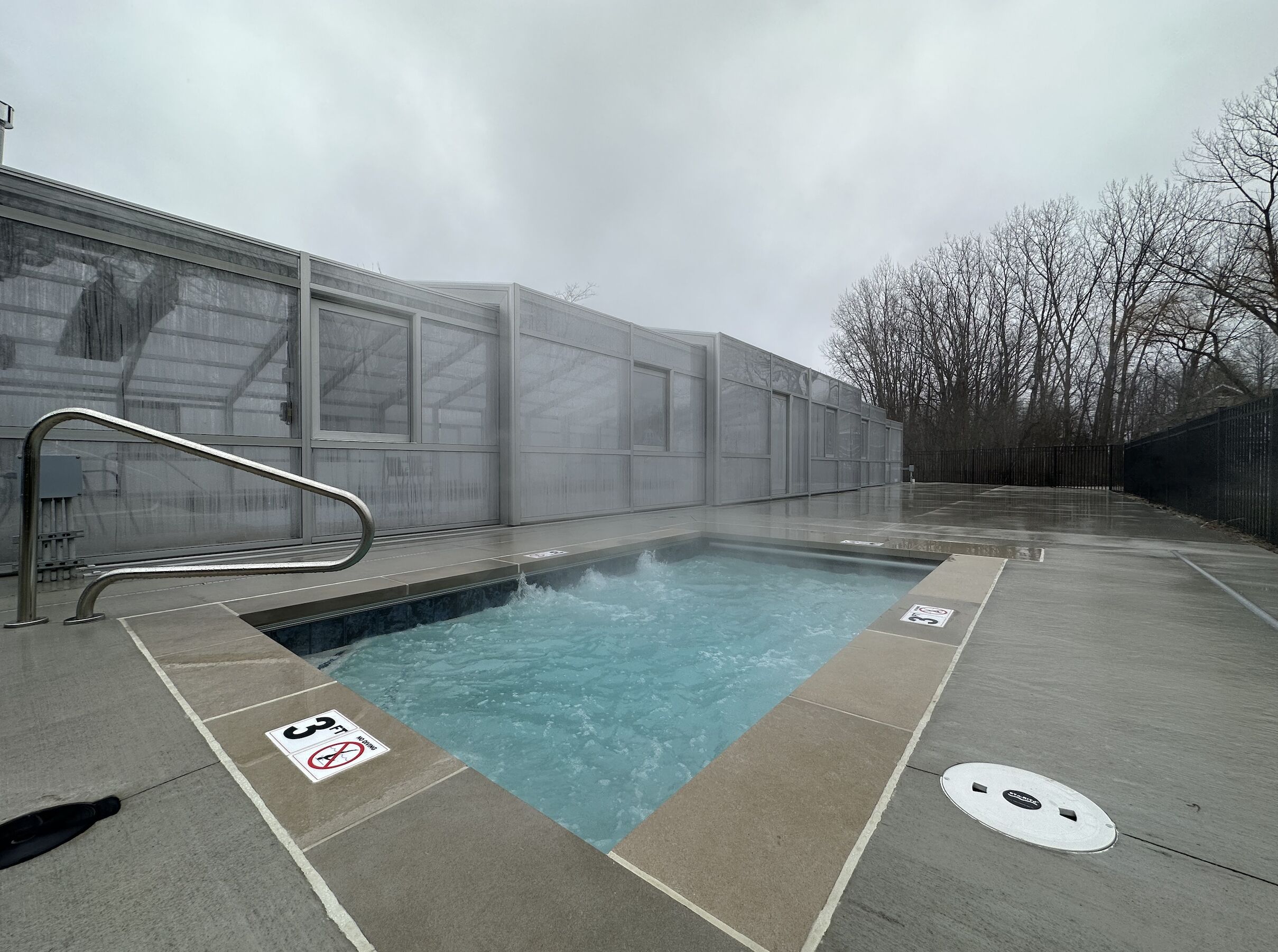 A swimming pool with a metal handrail, surrounded by a concrete deck.