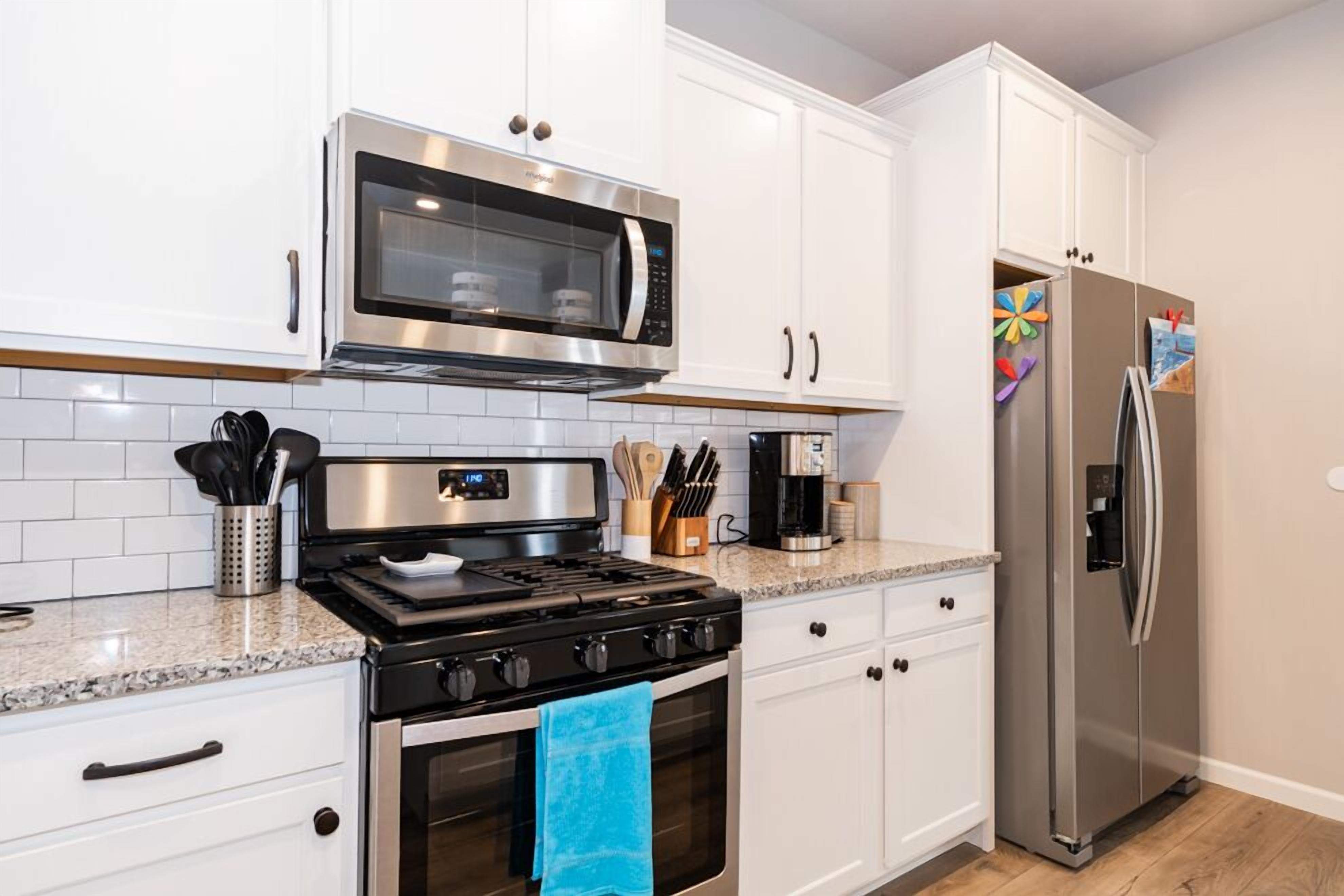 A modern kitchen with white cabinets, a stainless steel microwave, a gas stove, and a refrigerator.
