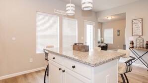 A kitchen with a granite countertop, white cabinets, and pendant lighting.