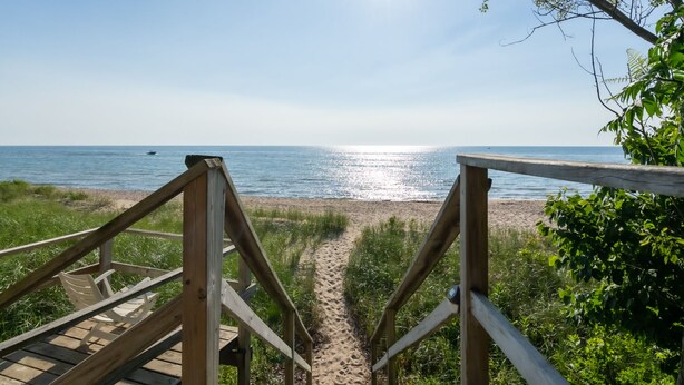 En trætrap fører ned til en strand med kig til havet.