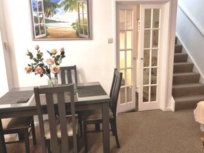A dining area with a table and chairs, a vase with flowers, a door with glass panels, and a staircase.