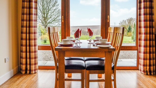 A dining table with chairs, set for four, in a room with large windows. - 2 bedroom accommodation in Blairgowrie (Blairgowrie)