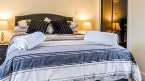 A neatly made bed with striped bedding, two pillows, and two folded towels. There are two bedside lamps and a nightstand with a lamp. - 2 bedroom accommodation in Blairgowrie (Blairgowrie)