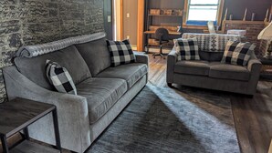 Ein modernes Wohnzimmer mit zwei grauen Sofas, einem gemusterten Teppich und einer Steinwand.