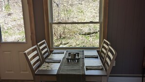 Ein Esstisch mit vier Stühlen, eine Ablage mit Tasse und Untertasse sowie ein Fenster mit Blick auf Bäume und einen Weg.