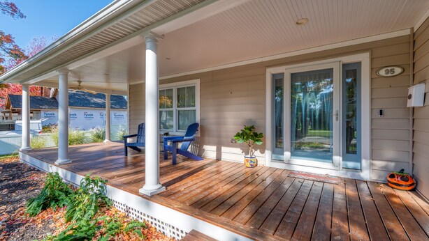Eine überdachte Veranda mit Holzterrasse, einem blauen Stuhl, einem kleinen Tisch und einem Blumentopf.