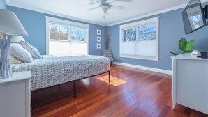 Ein Schlafzimmer mit Bett, Schreibtisch, Deckenventilator und großen Fenstern.