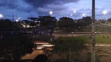 Vista noturna de uma ponte iluminada por postes, um carro estacionado e uma área gramada com uma placa.