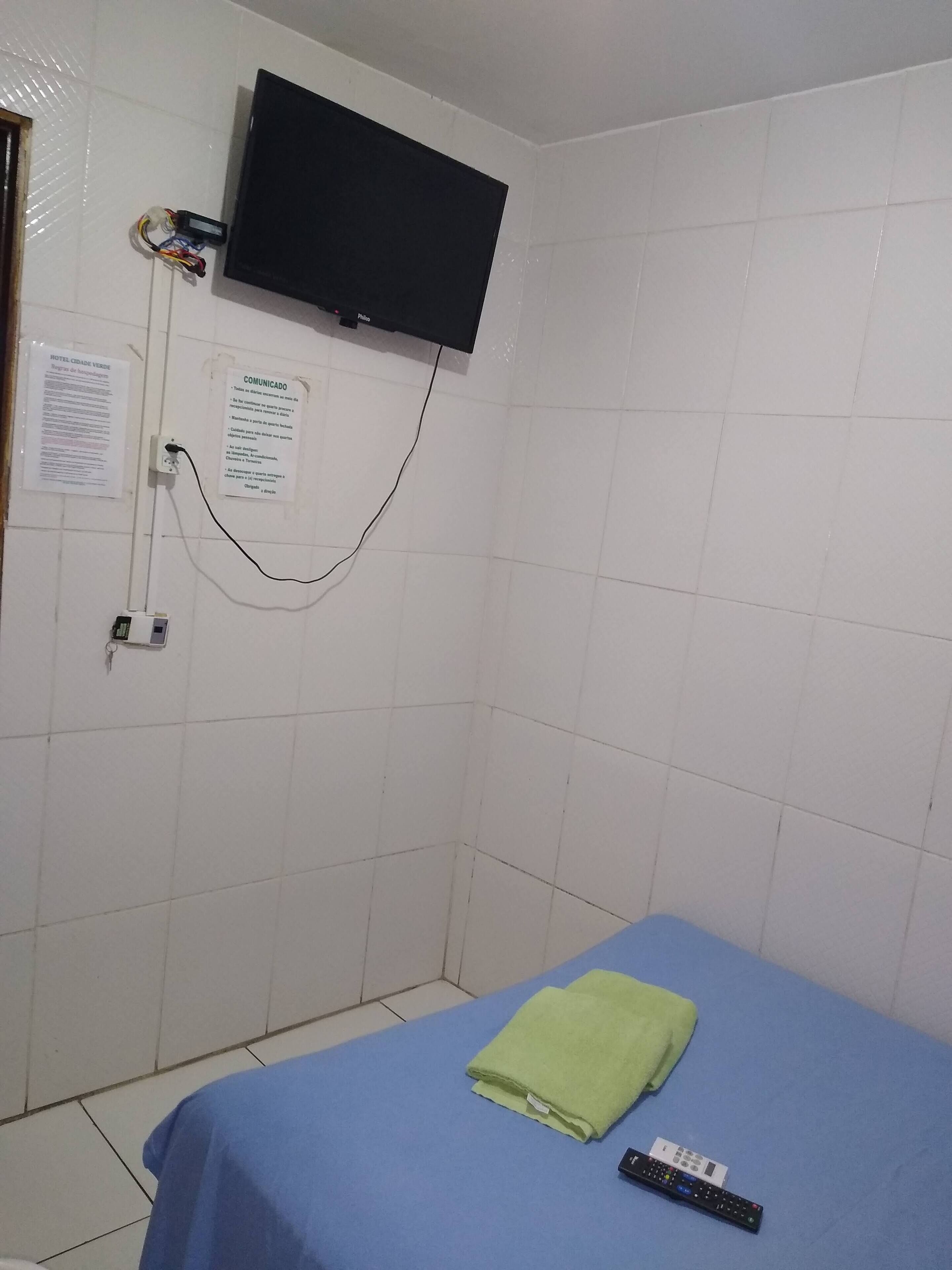 Une petite pièce comprenant un lit, un téléviseur fixé au mur et un panneau d’information.