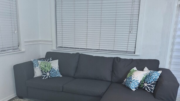 A living room with a dark grey sectional sofa, patterned rug, and white walls. - 15 MINUTES WALK TO THE BEACH (Nassau)