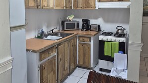 A compact kitchen with wooden cabinets, a microwave, a stove, and a sink. - 15 MINUTES WALK TO THE BEACH (Nassau)