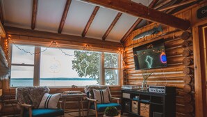 L’intérieur chaleureux d’un chalet, avec un décor en bois, un téléviseur fixé au mur et une vue sur l’extérieur grâce à de grandes fenêtres.
