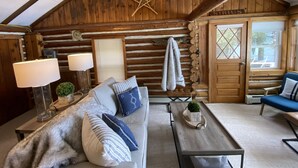 L’intérieur d’un chalet confortable, avec un plafond en bois, un canapé agrémenté de coussins à motifs, une table basse et une fenêtre offrant une belle vue.