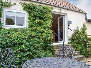A house with a white exterior, a tiled roof, and a door leading to a kitchen. There is a small staircase with a metal railing leading to the door. - The Sheep Shed - UK38437 (Bridlington)