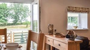 Ein Essbereich mit Holztisch, Stühlen, einer Schüssel, einer Kanne und einem Fenster mit Blick auf Grünflächen.