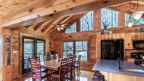 A wooden cabin interior with a dining area, kitchen, and large windows. - Expansive Lake Front Log Cabin/Easy Walk to Private! (Jacksboro)