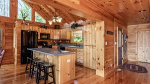A wooden cabin with a kitchen featuring a central island, bar stools, and a dining table. - Expansive Lake Front Log Cabin/Easy Walk to Private! (Jacksboro)