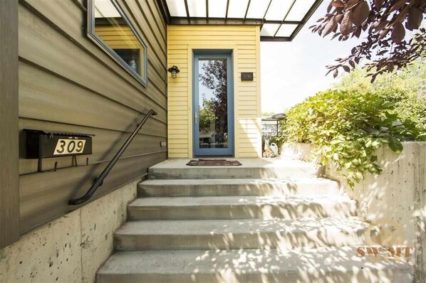 Stunning home with a concrete staircase leading to a front door, surrounded by lush greenery and a beautiful tree.