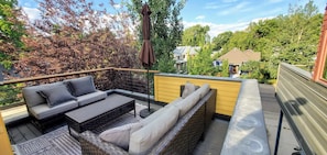 Relax on the outdoor patio with a sofa, wicker bench, and small table, surrounded by lush greenery.