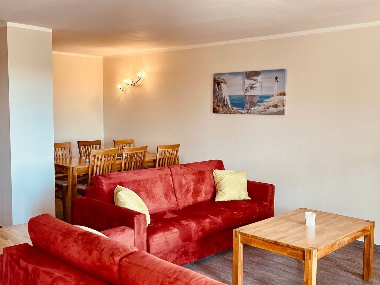 Una sala de estar con un sofá rojo, una mesa de comedor de madera y sillas. Hay un cuadro en la pared.