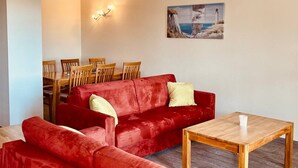 A living room with a red sofa, wooden dining table, and chairs. There is a painting on the wall. - Vacation resort Süderhof (Breege)
