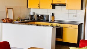 A compact kitchen with yellow cabinets, a built-in oven, and a coffee maker. - Vacation resort Süderhof (Breege)