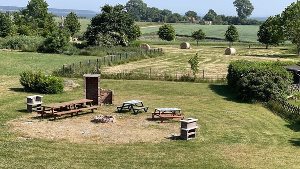 A picnic area with benches and tables in a grassy field, surrounded by trees and hay bales. - Vacation resort Süderhof (Breege)