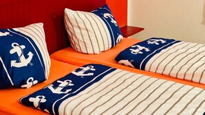 A bed with striped bedding and pillows featuring nautical designs. - Vacation resort Süderhof (Breege)