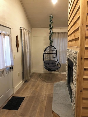 A room with a hanging chair, a fireplace, and a door with a towel rack. - Owl's Tale at Avenwood Cabins (New Straitsville)